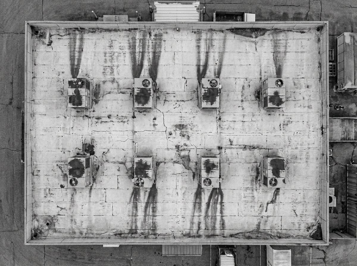 Illustrative: overhead survey view of an aging commercial roof, oil and rust streaks running from each of its package HVAC units
